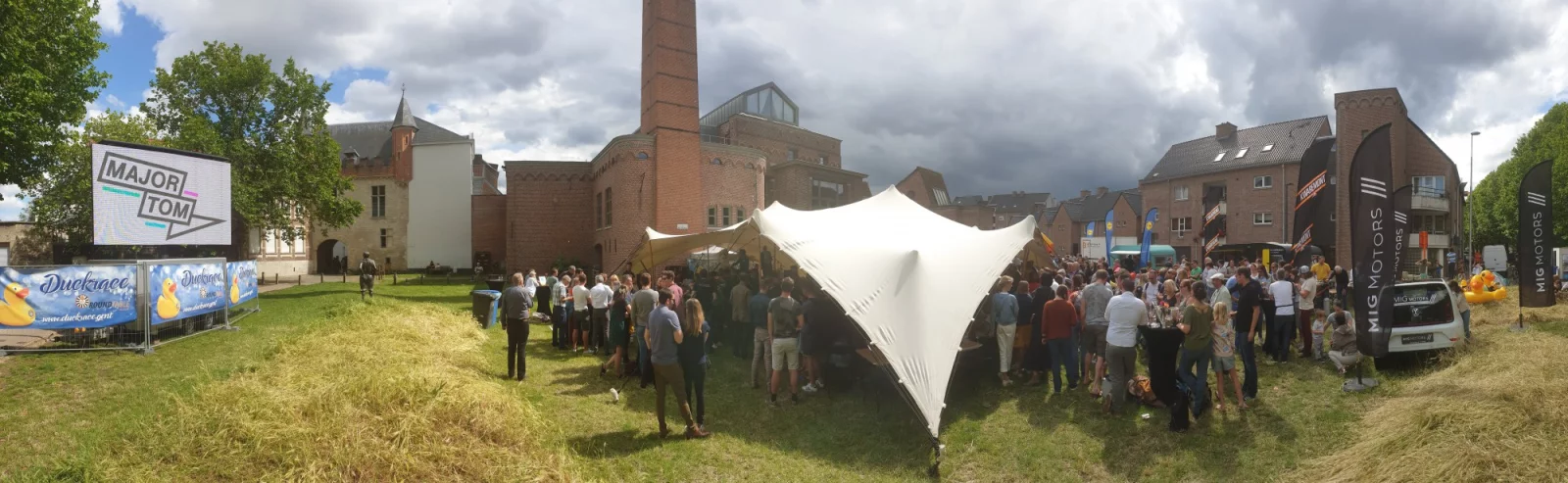 Panorama of the Duck Race village in Ghent, with a large tent, visitors and a screen showing the Major Tom logo