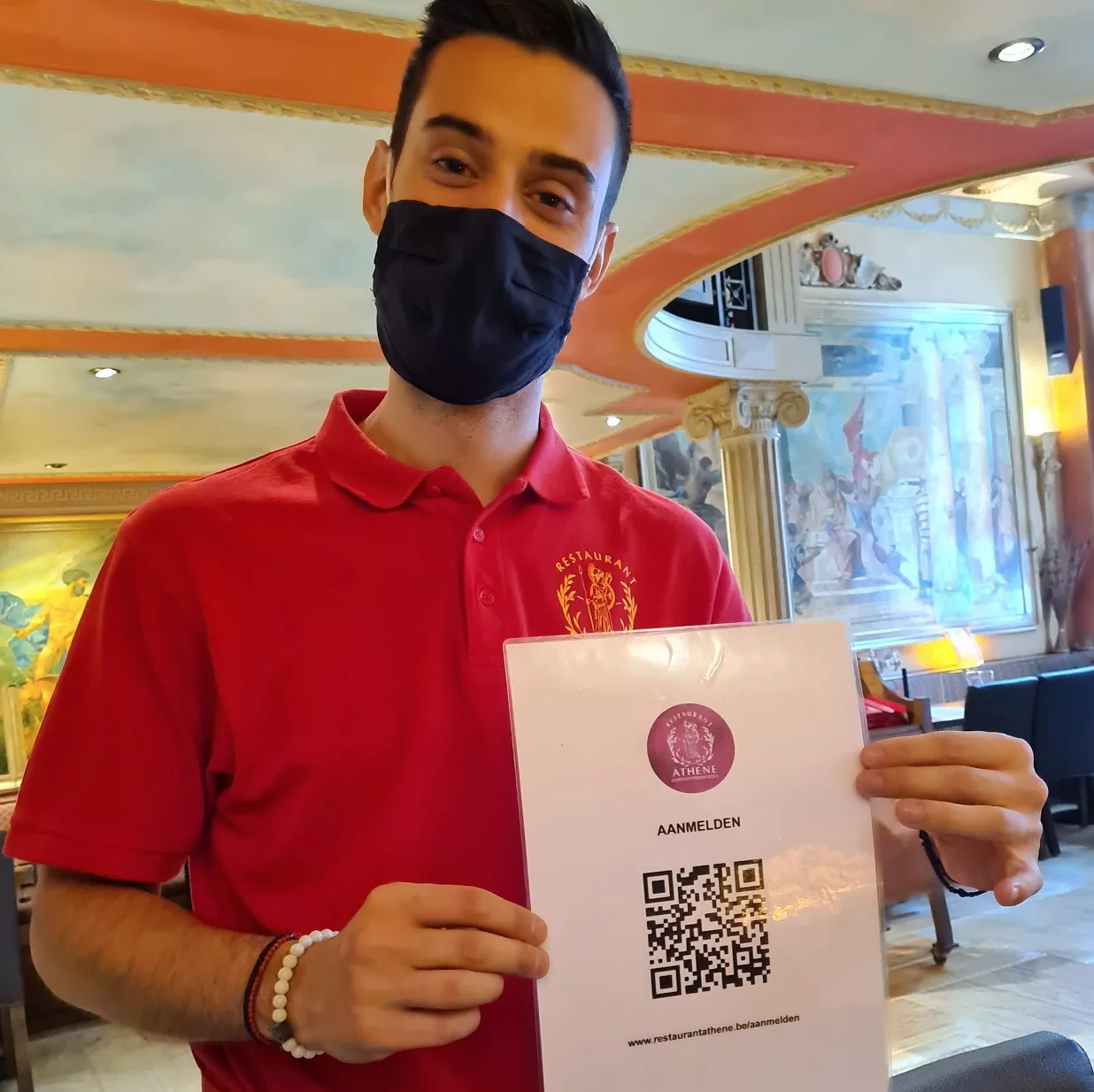 A waiter at restaurant Athene, wearing a face mask, holds up a card with the QR code to sign in