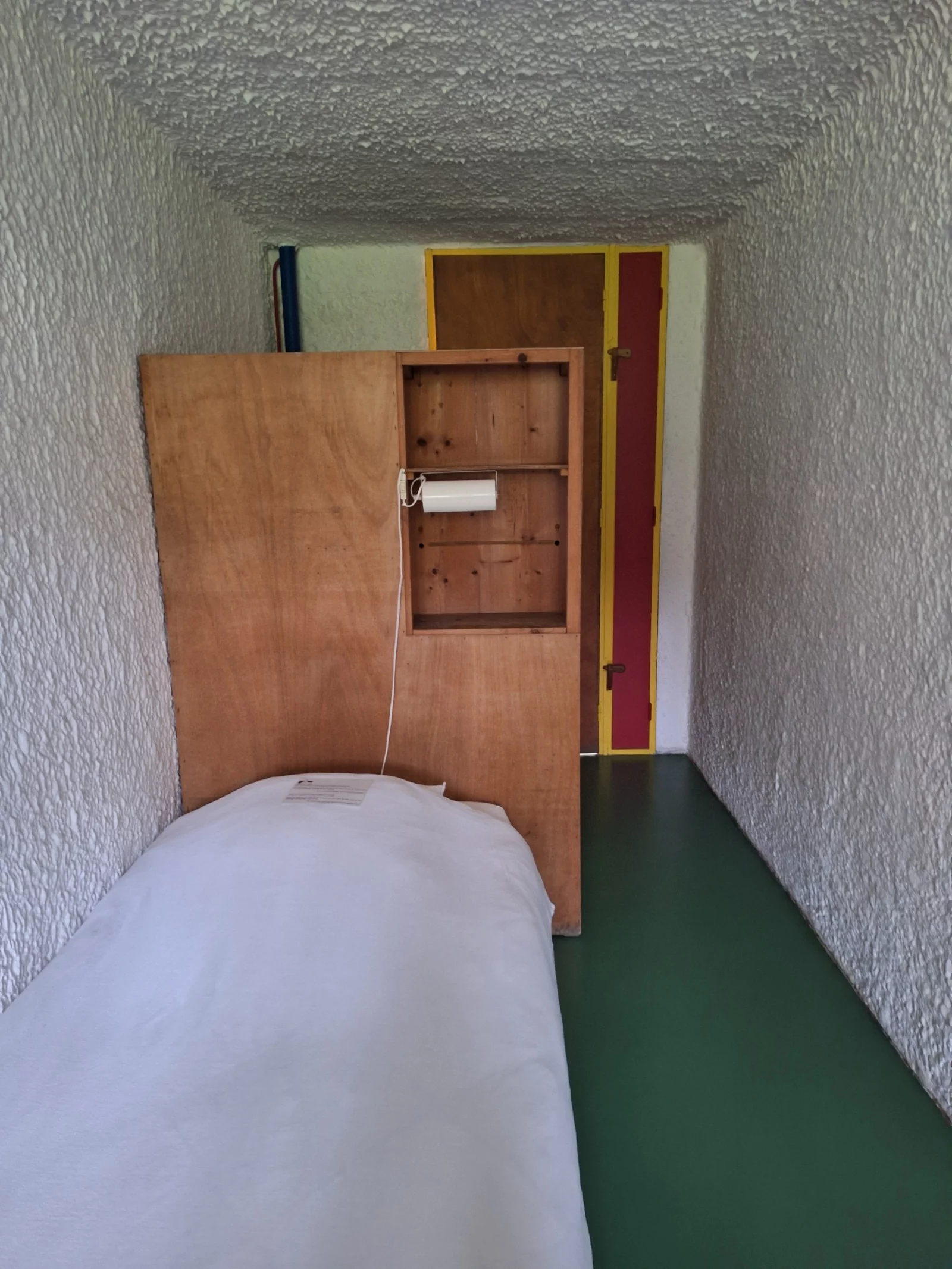 Een cel: bed, wandkast, groene vloer