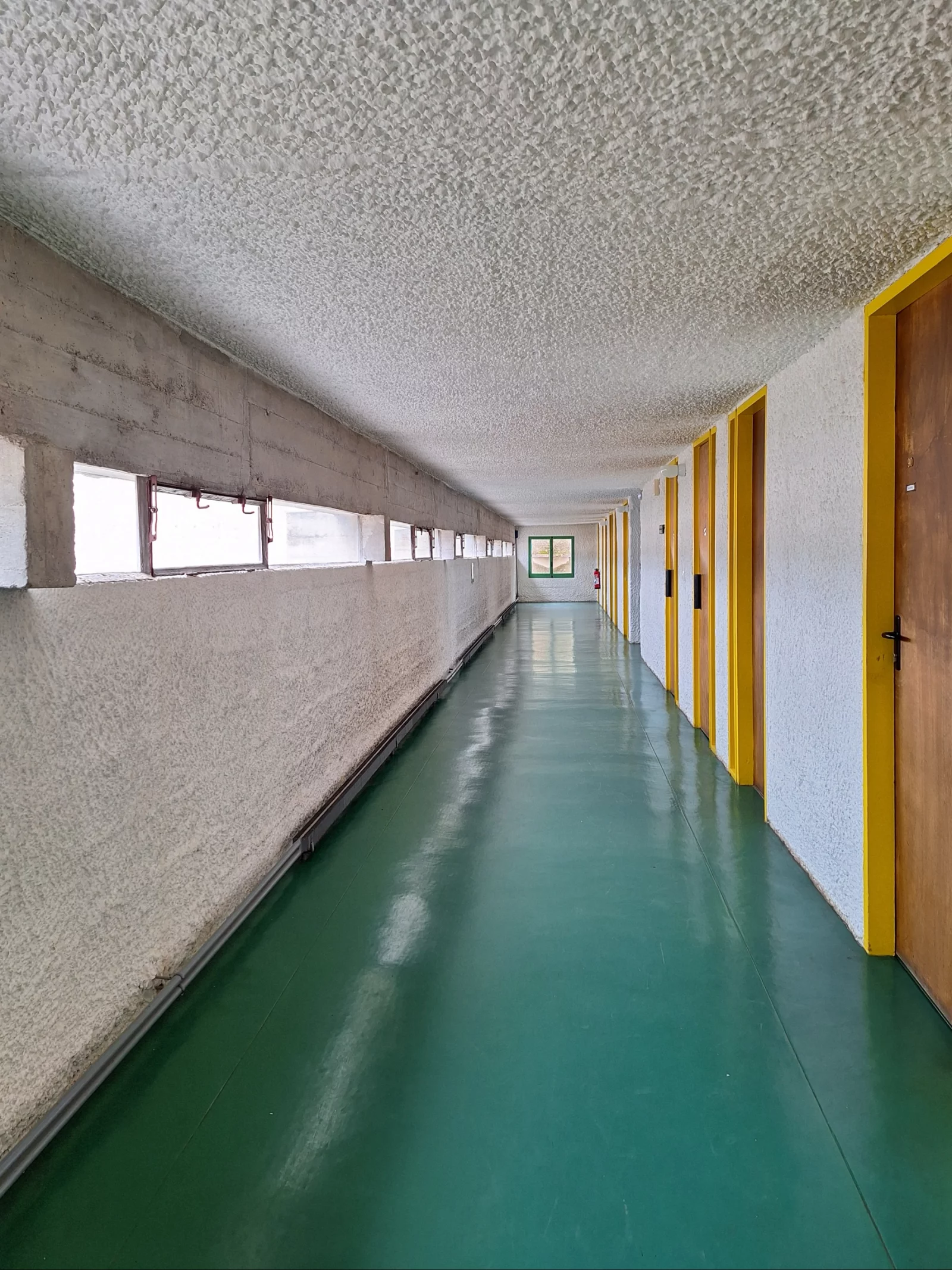 De gang met de deuren van de cellen, groene vloer en gele deurlijsten