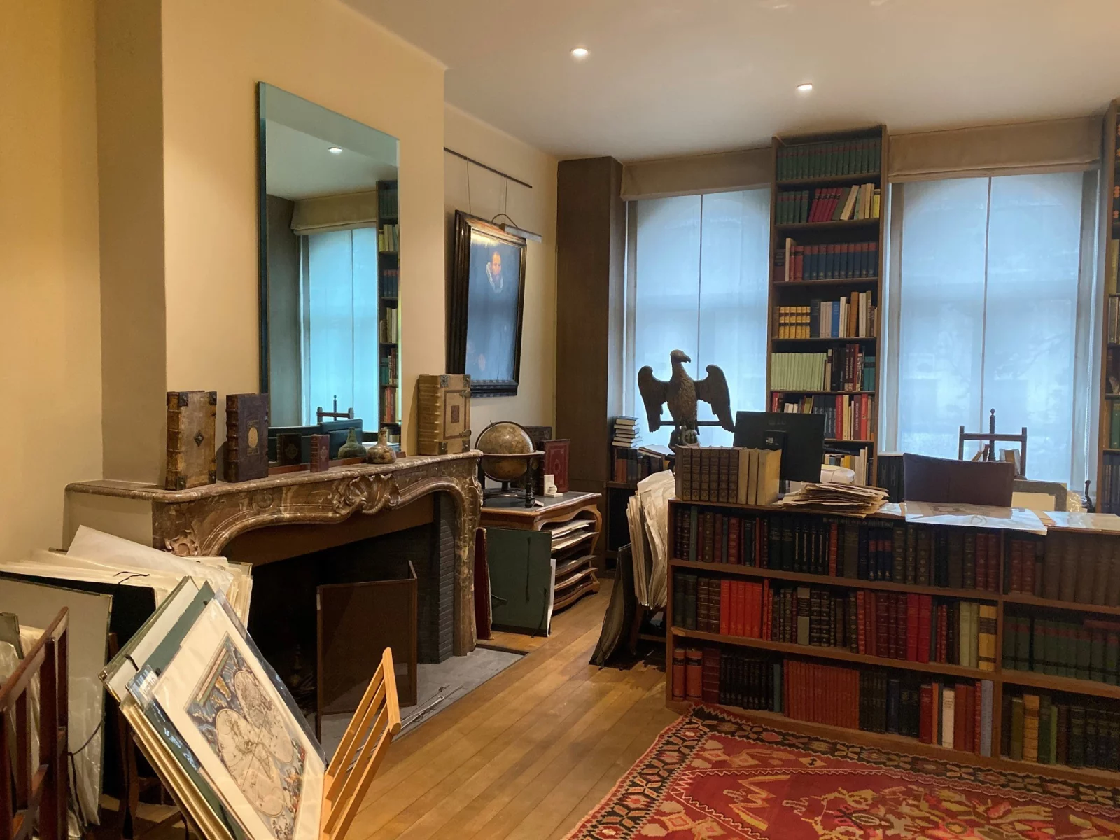 The interior of the Sanderus antiquarian bookshop: bookcases up to the ceiling, a mantelpiece with a globe, a wooden eagle and framed antique maps against the wall