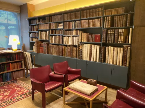 De winkel van Antiquariaat Sanderus in Gent: een wand vol oude boeken in leren banden, twee bordeauxrode fauteuils en een perkamenten folio op de salontafel
