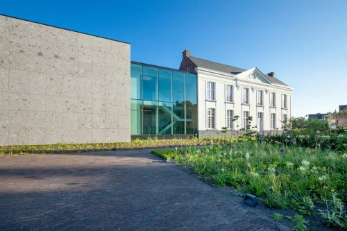 The office building of project G01: a renovated white presbytery with a glass link and a natural stone extension, with a flower meadow in front