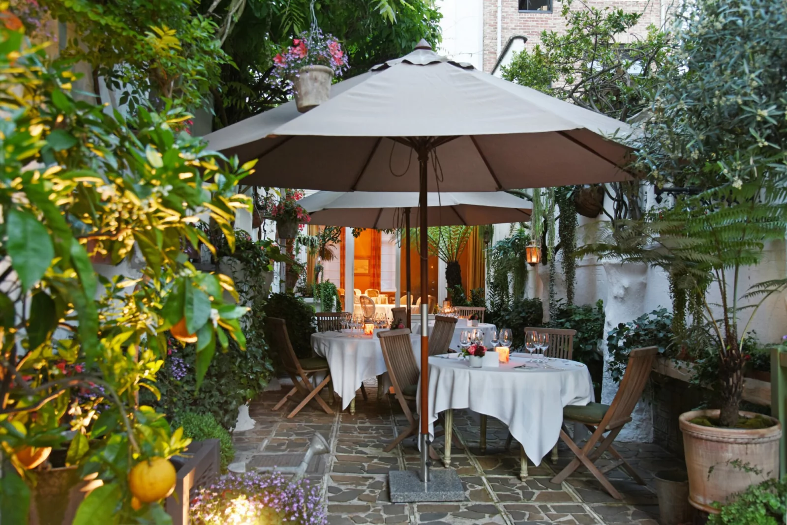 Het tuinterras van restaurant Jan Van den Bon bij avondlicht, met gedekte tafels onder een parasol