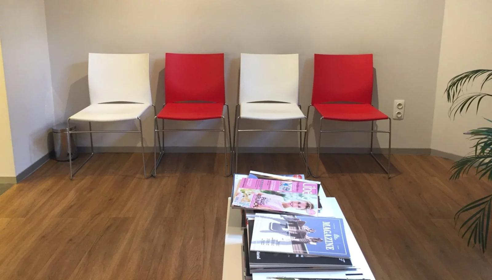 De wachtzaal van Huisartsen 't Zuid: vier stoelen in wit en rood tegen de muur, met een stapel tijdschriften op de tafel ervoor