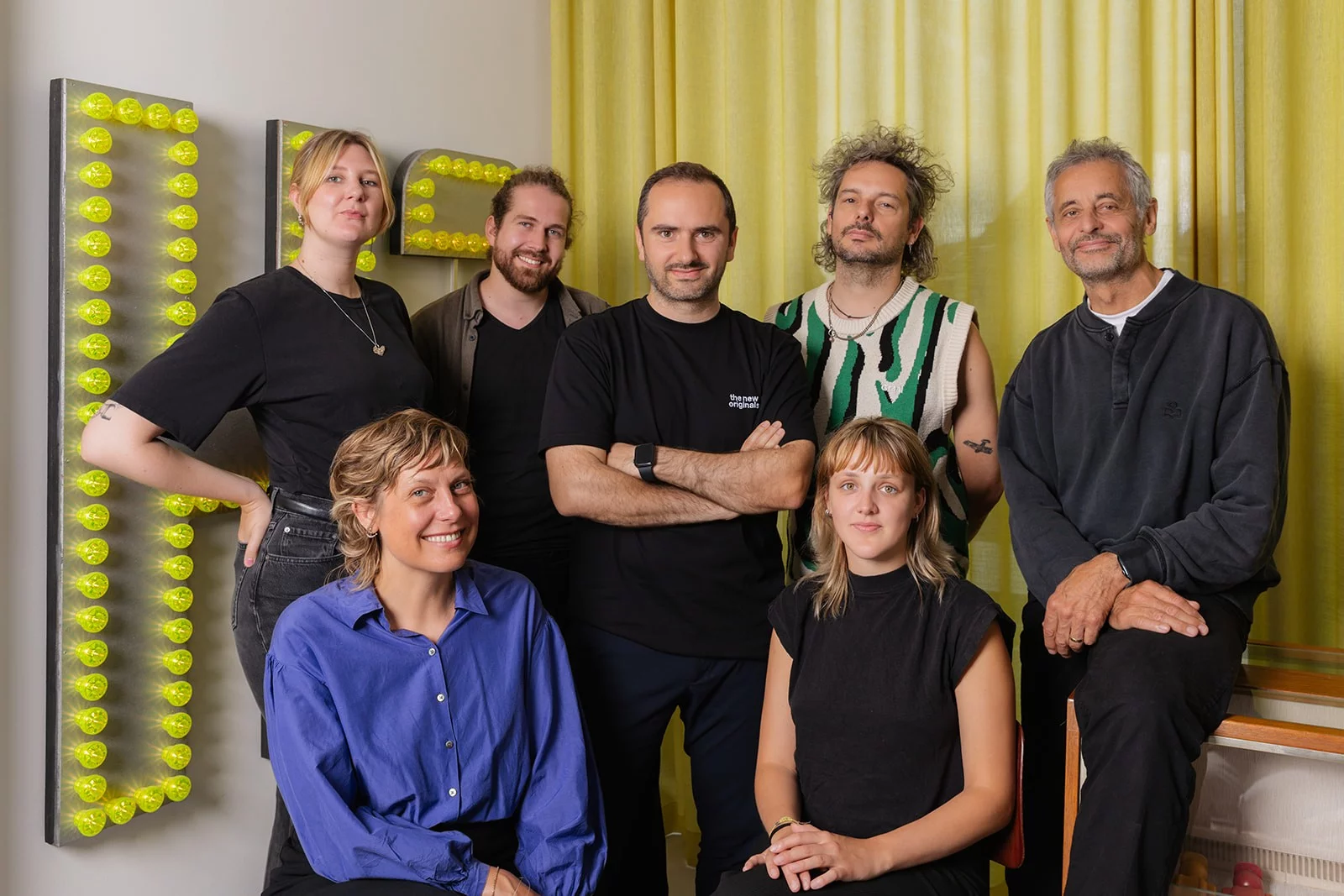 The Pi&egrave;ce Mont&eacute;e team in their studio, in front of a wall of yellow light-up letters