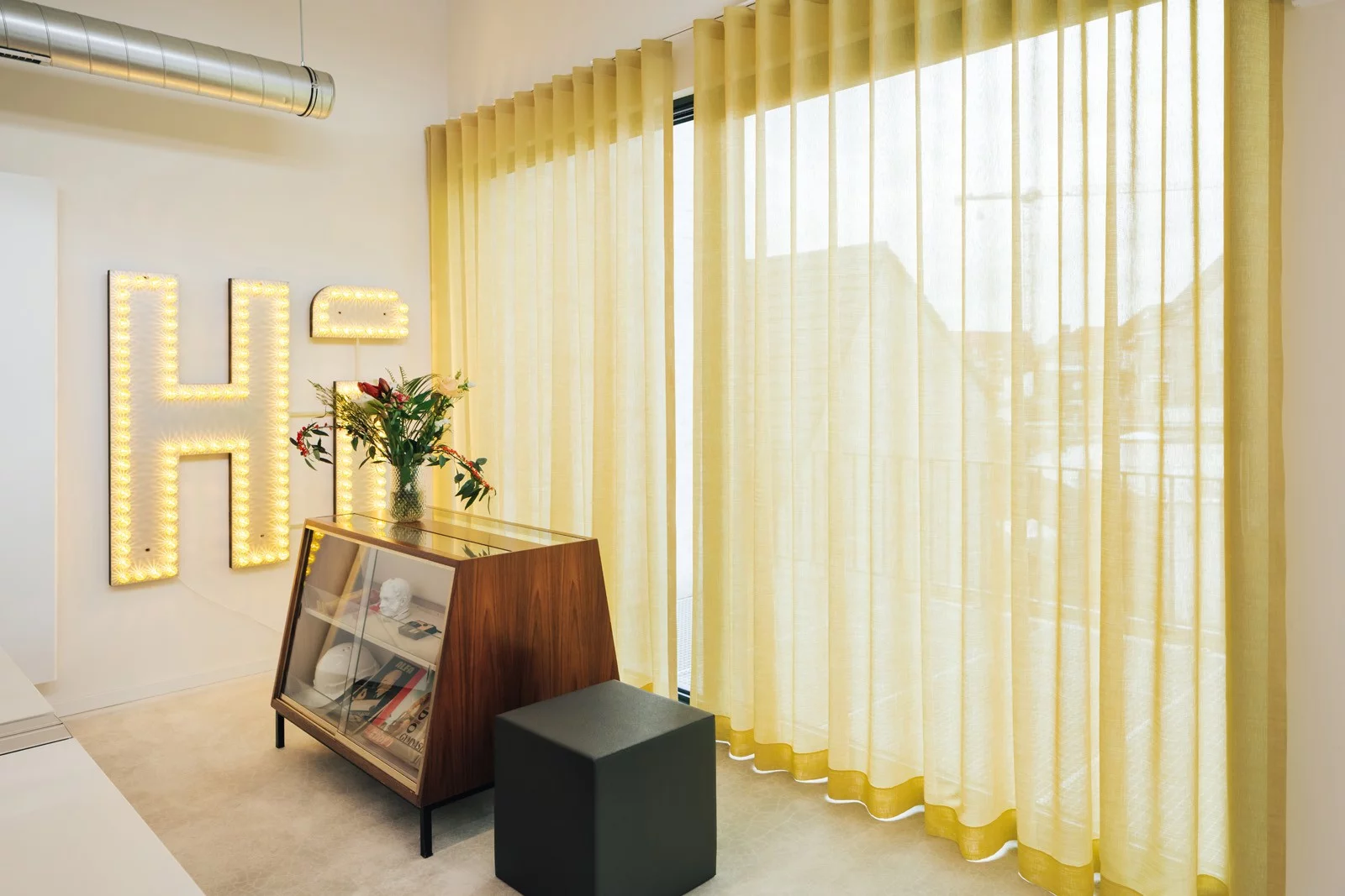 The Pi&egrave;ce Mont&eacute;e office in Ghent with yellow curtains, a display cabinet and a large light-up letter H