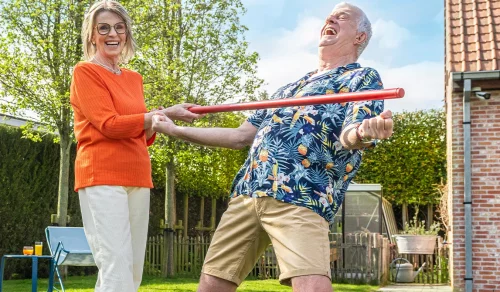 Two seniors playing limbo with a red bar in the garden