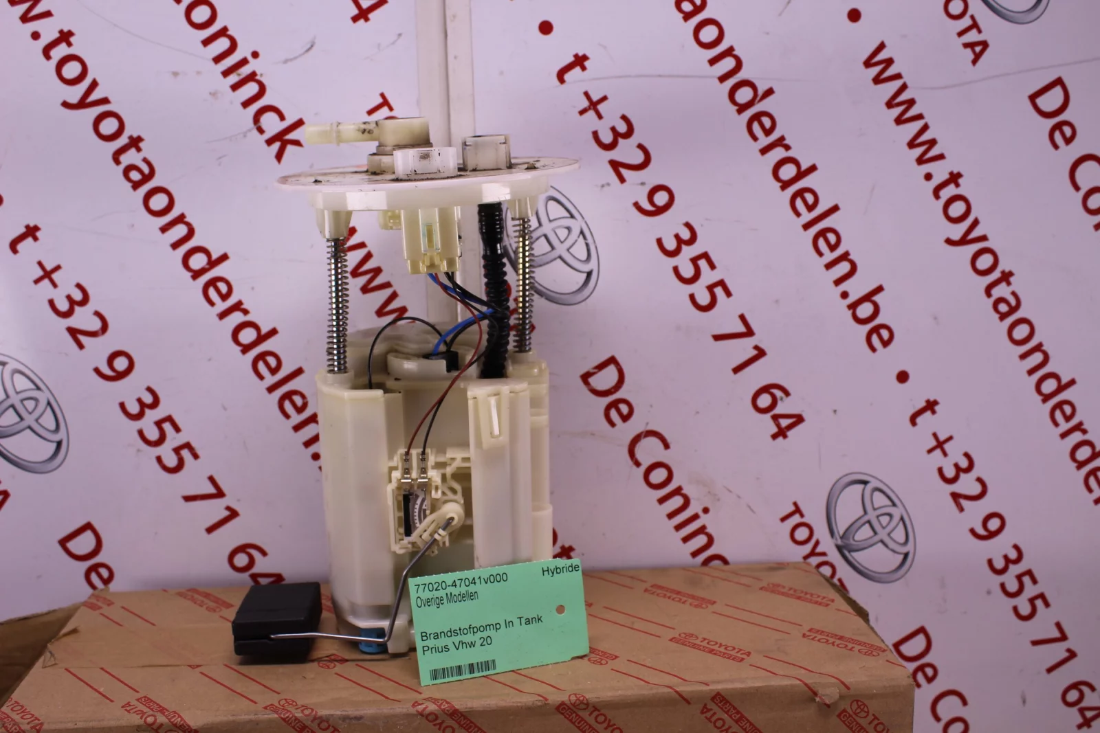 A dismantled fuel pump in front of the printed wallpaper, with a green printed card showing article number, model and barcode leaning against it