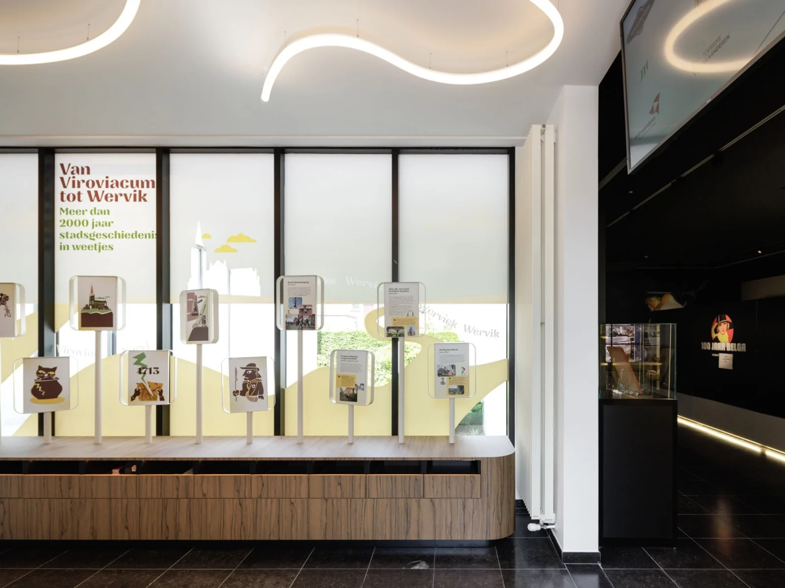 The desk of the tourist welcome centre in Wervik with a staff member, wooden walls and the town logo